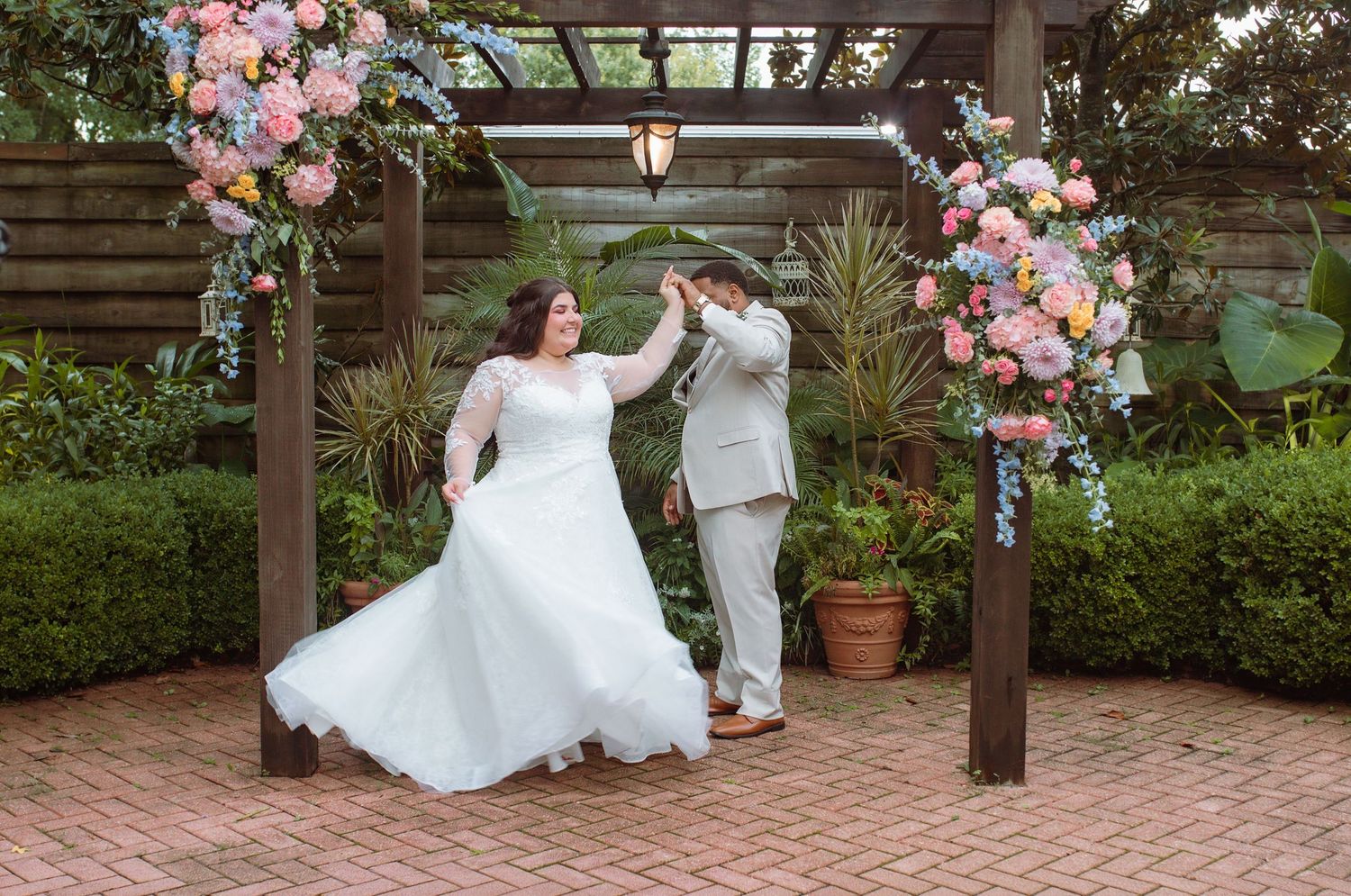 Bride and groom dancing under a floral pergola arch with pink and blue blooms at an outdoor garden wedding.