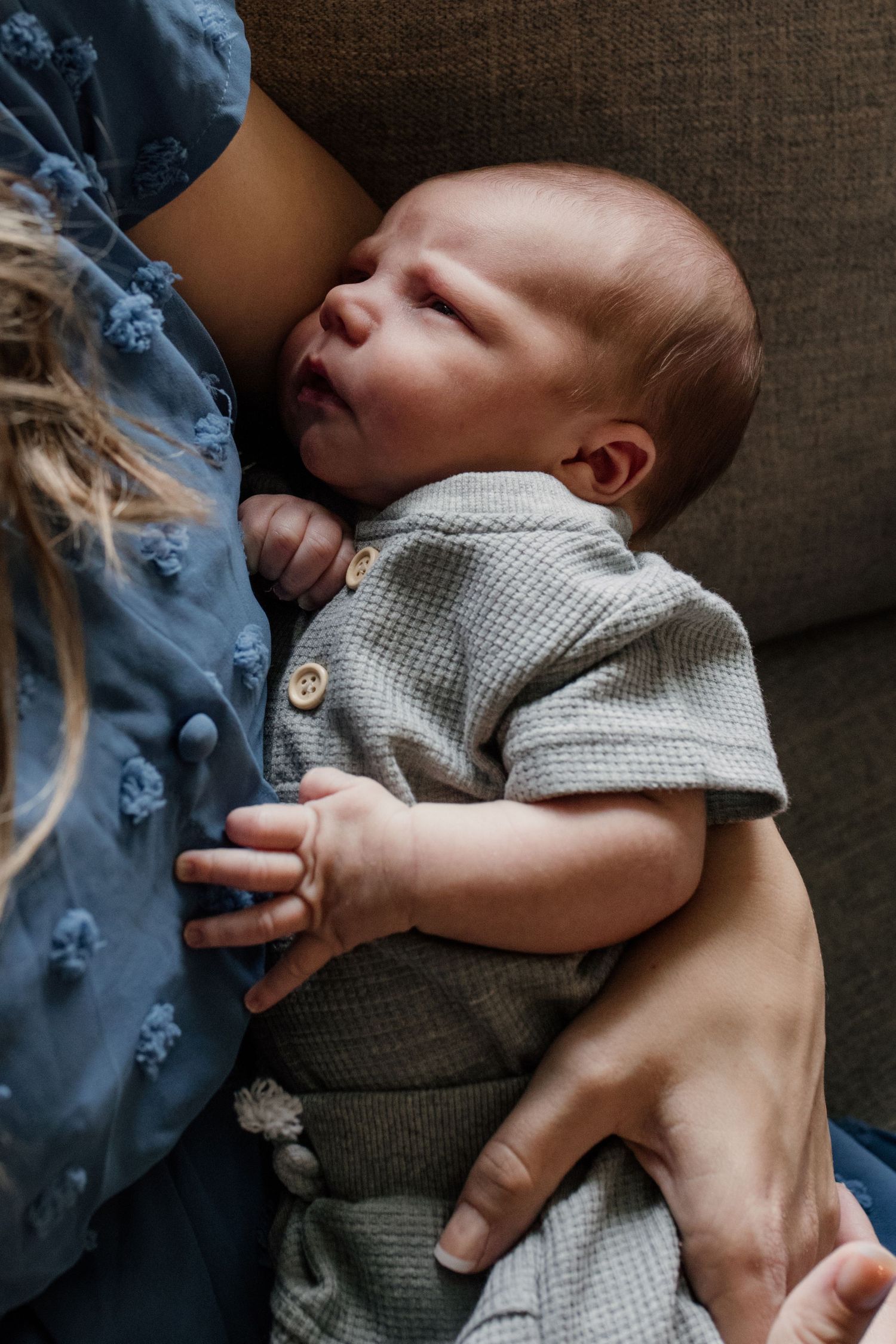Close-up of a peaceful newborn baby in a gray knit outfit being held in loving arms.