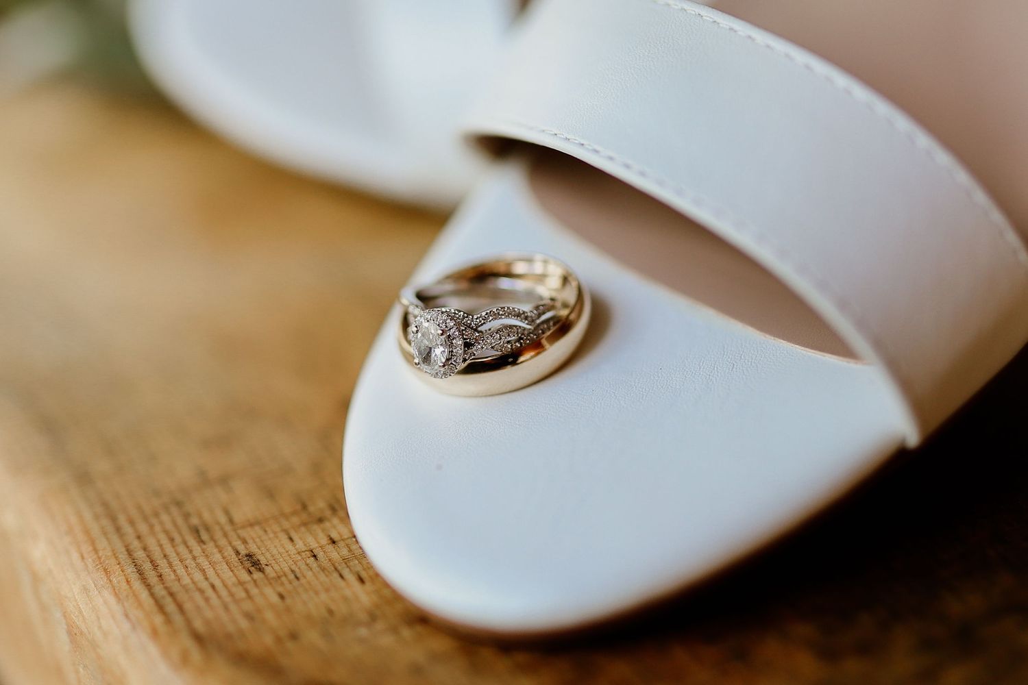 Gold diamond engagement ring and wedding band resting inside a white bridal heel on a wooden surface.