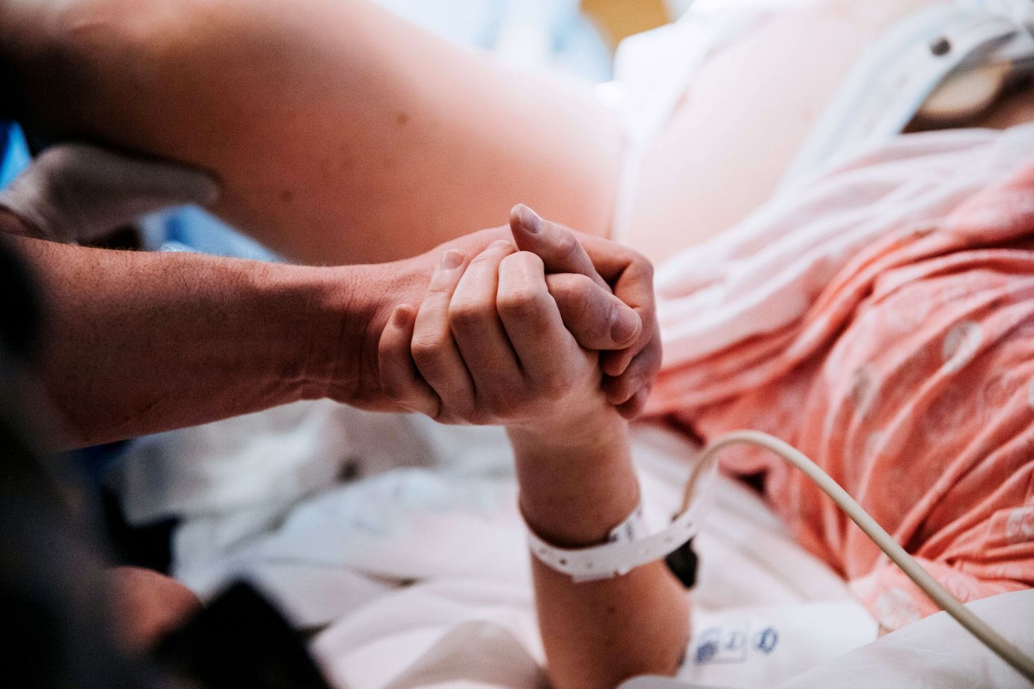 Partner holding laboring womans hand in hospital bed during childbirth for emotional support.