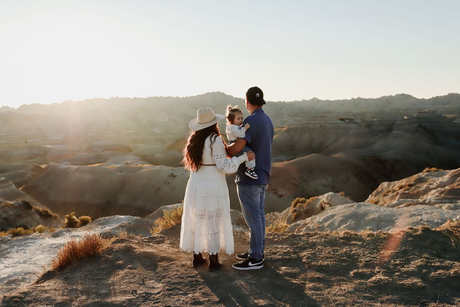 Family of three standing together at golden hour in stunning badlands desert landscape at sunset.