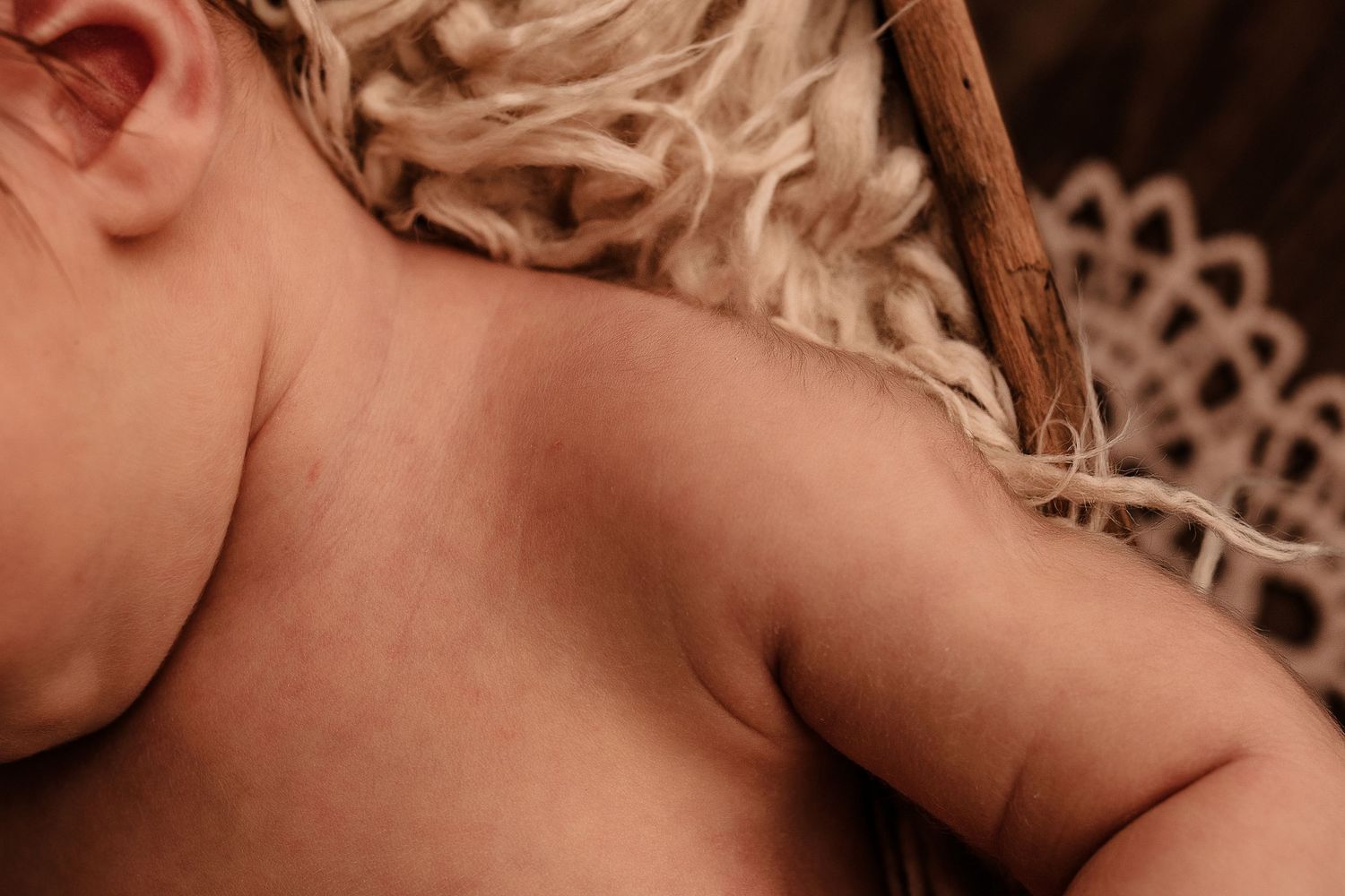 Close-up of a newborn baby's soft shoulder and neck resting on a textured woven blanket.