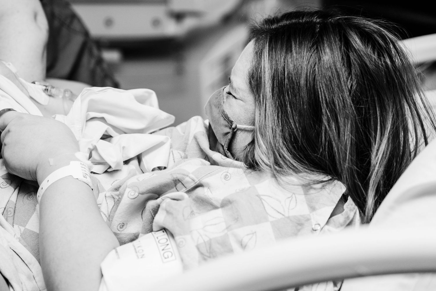 Black and white photo of someone lying in a hospital bed with white sheets and pillows, smiling with emotion.