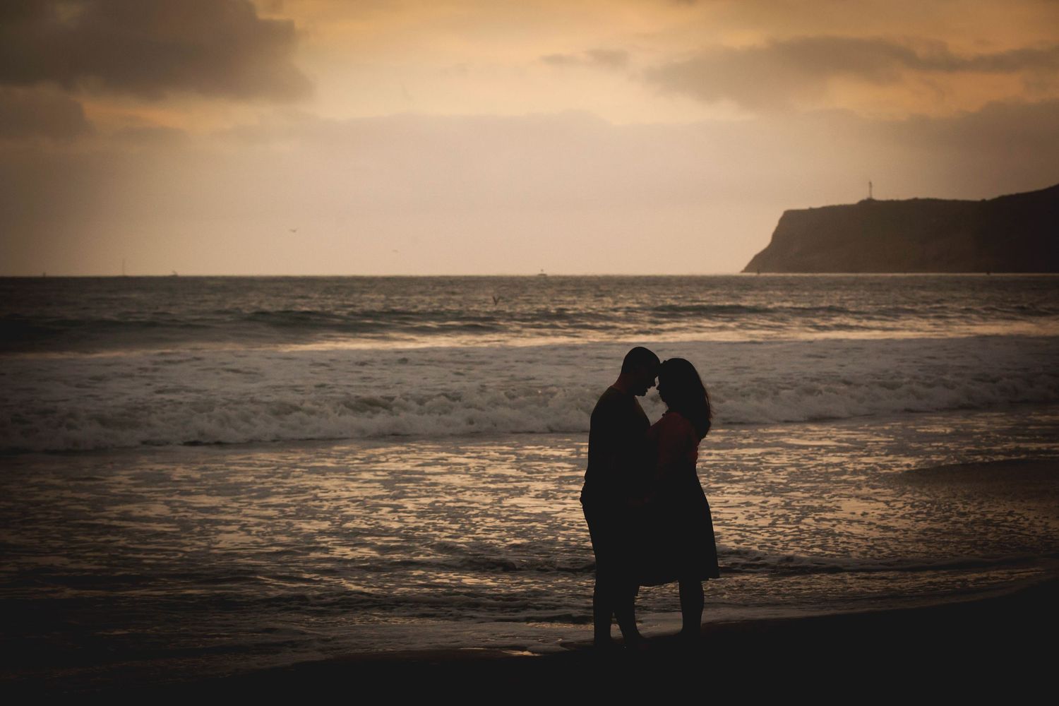 Romantic couple silhouetted against a dramatic sunset sky on the beach.