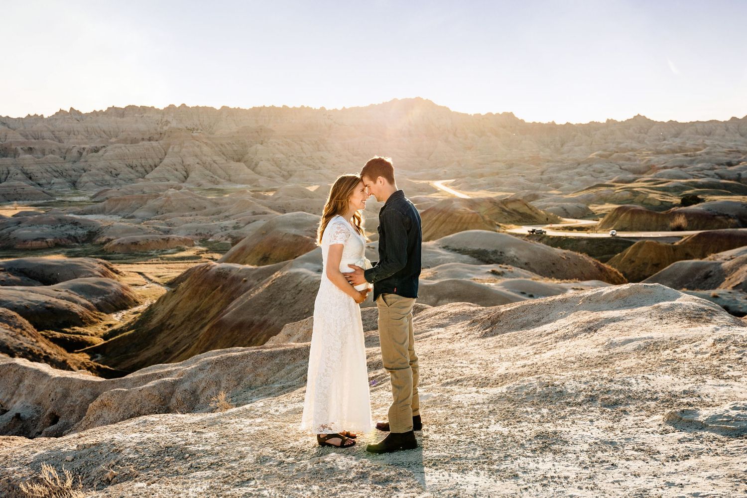 Couple standing face-to-face in white and denim at golden hour in rocky Badlands landscape.