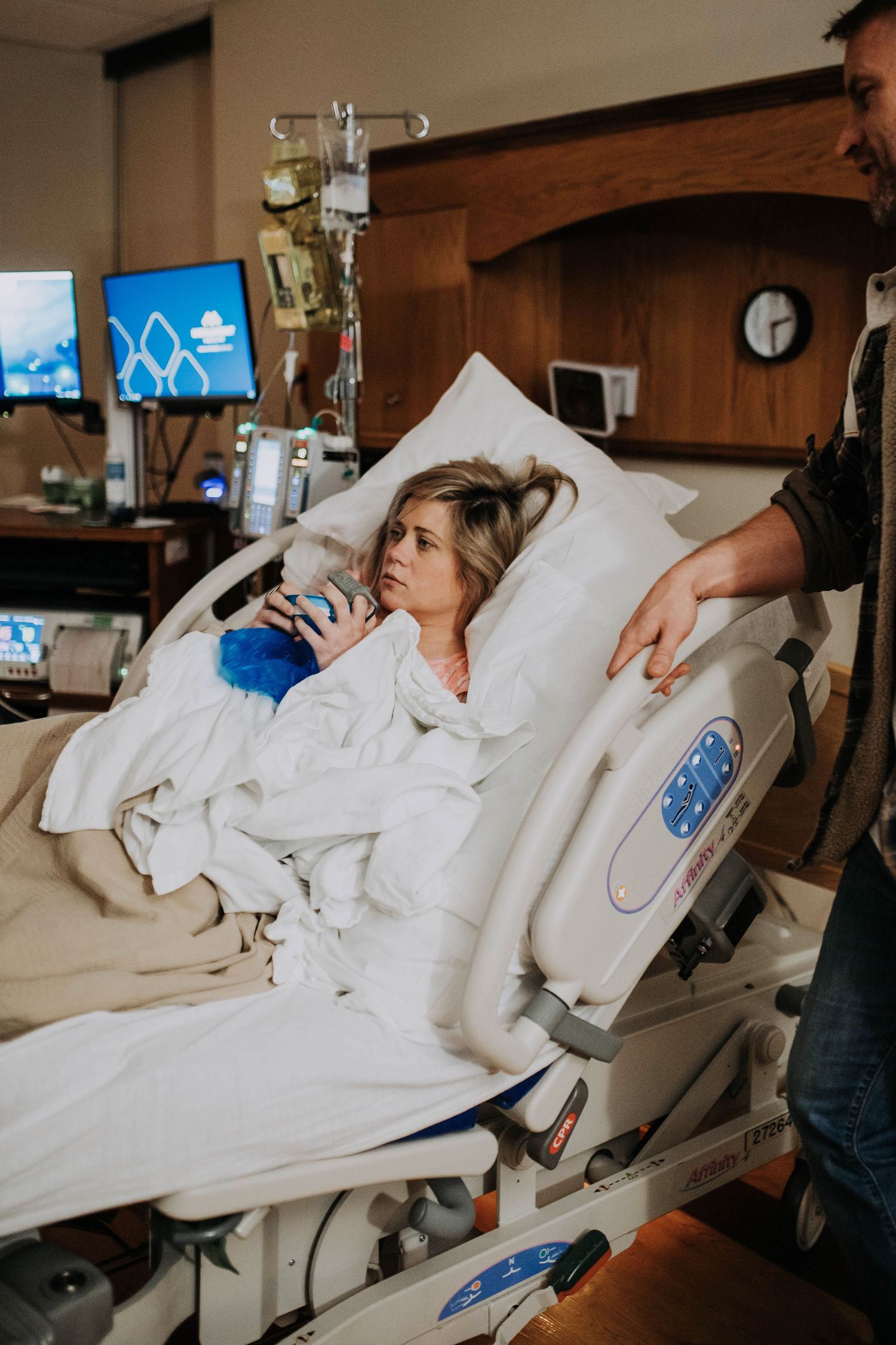 Woman resting in hospital bed during labor while partner stands supportively beside her.