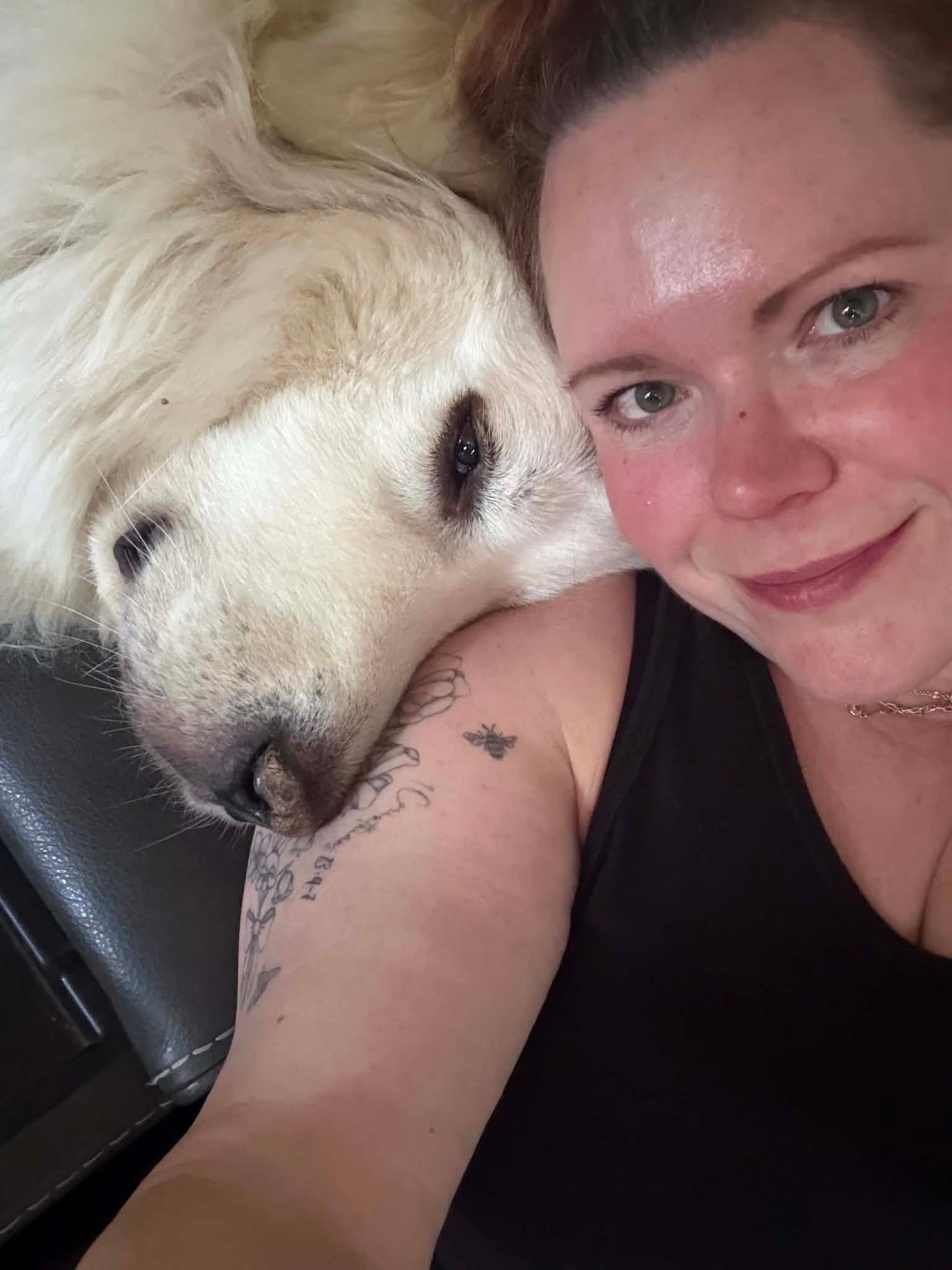 Woman taking a selfie with a large white fluffy dog resting its head on her shoulder, both lying down.
