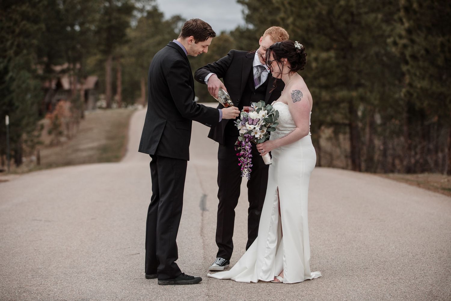 Bride and groom exchange rings with officiant on a scenic road during an outdoor wedding ceremony.