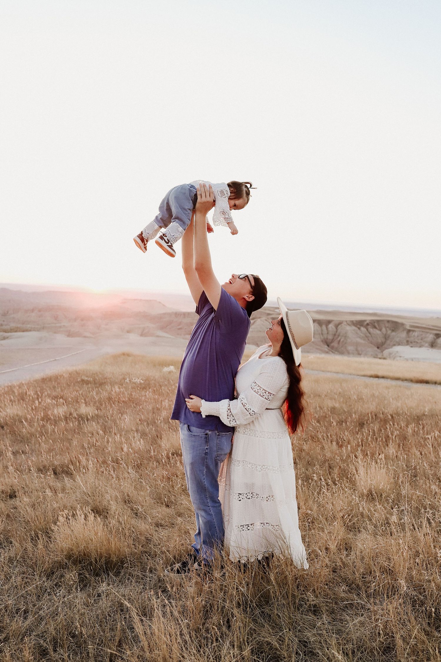 Parents lifting their baby joyfully in a golden field at sunset in a heartwarming family portrait.