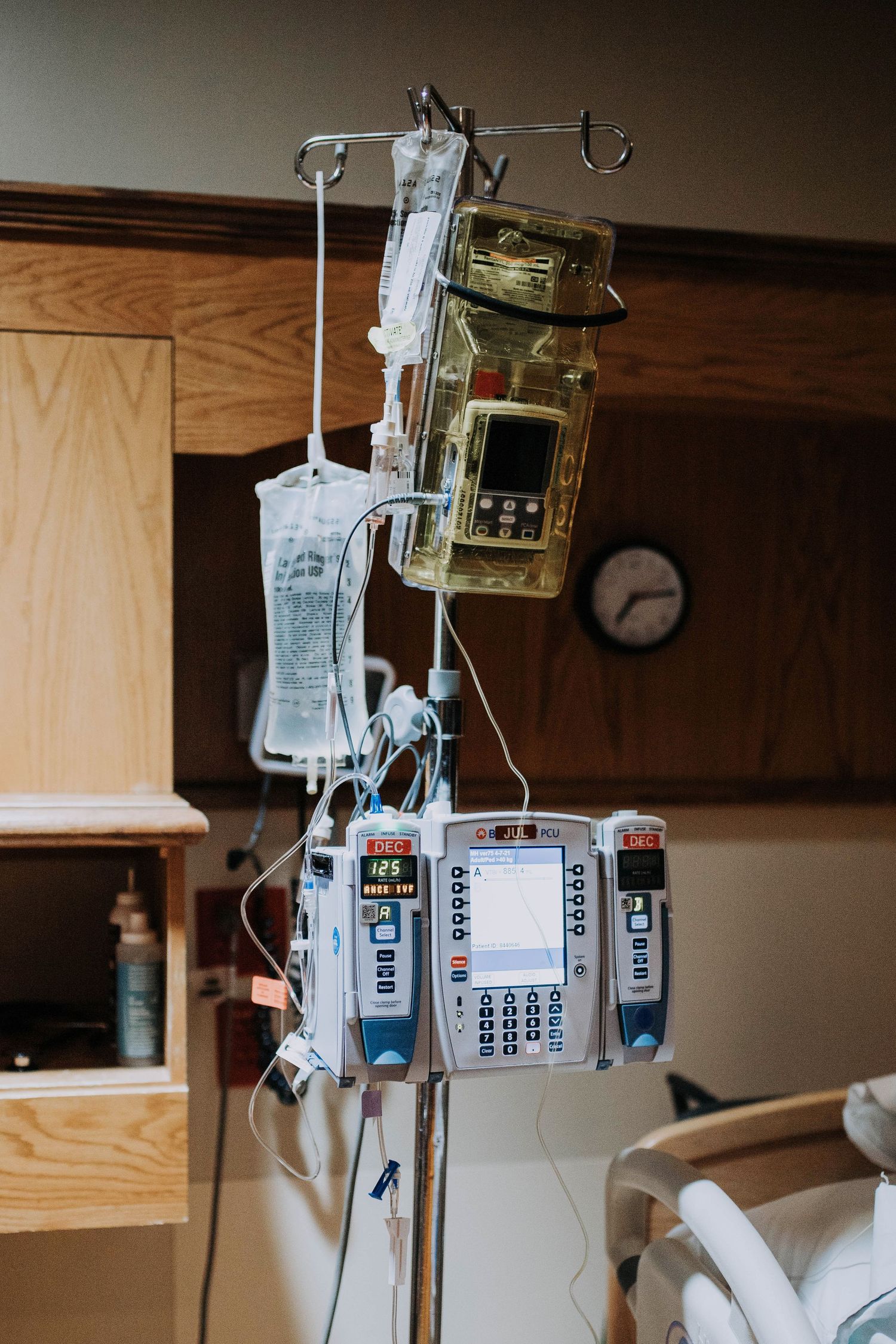 Hospital IV pole with multiple infusion pumps and fluid bags hanging in a patient room.
