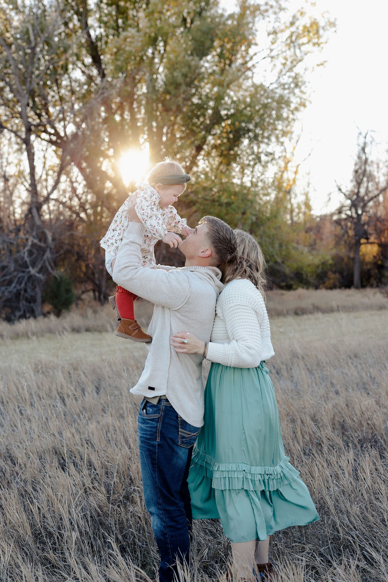 Parents lifting their baby at sunset in a golden meadow, sharing a tender family moment.