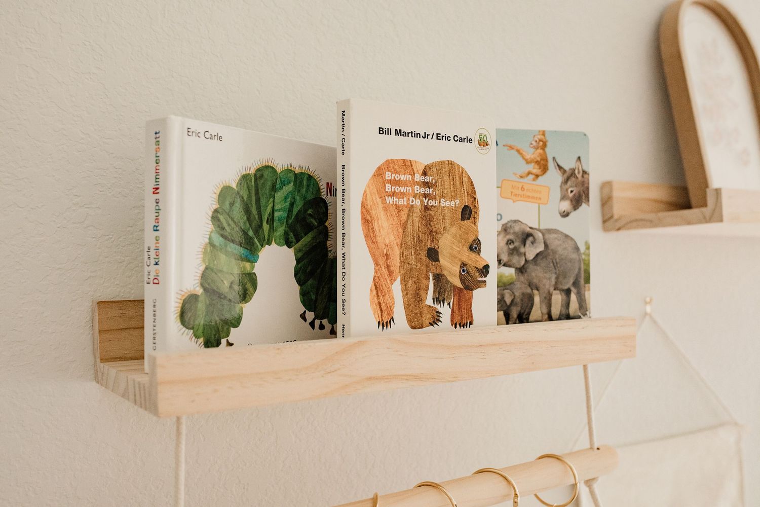 Wooden nursery bookshelf displaying Eric Carle board books including The Very Hungry Caterpillar and Brown Bear.