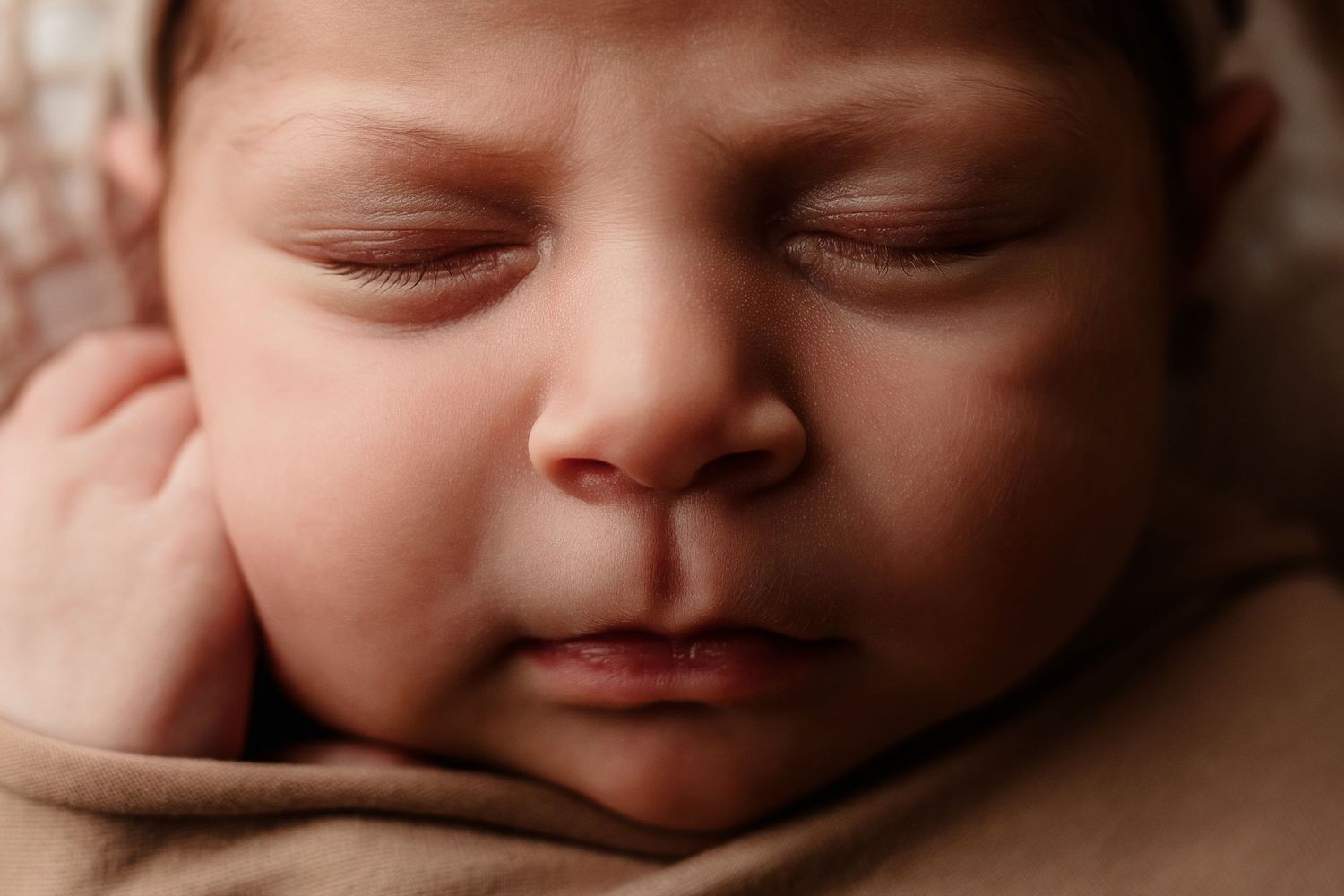 Peaceful sleeping newborn baby close-up portrait with soft skin and tiny hand near face.