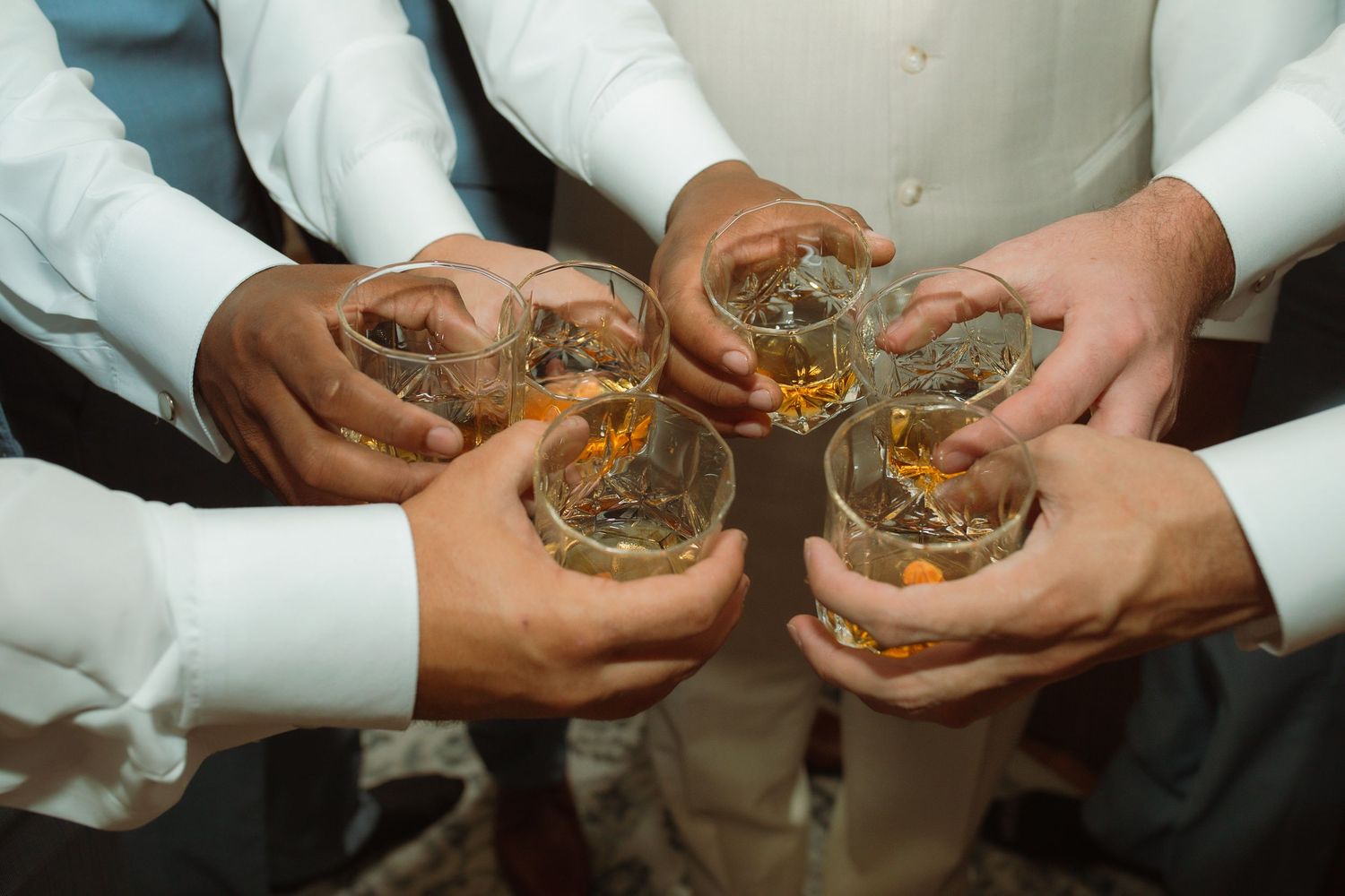 Group of men in white shirts toasting with glasses of whiskey at a wedding celebration.