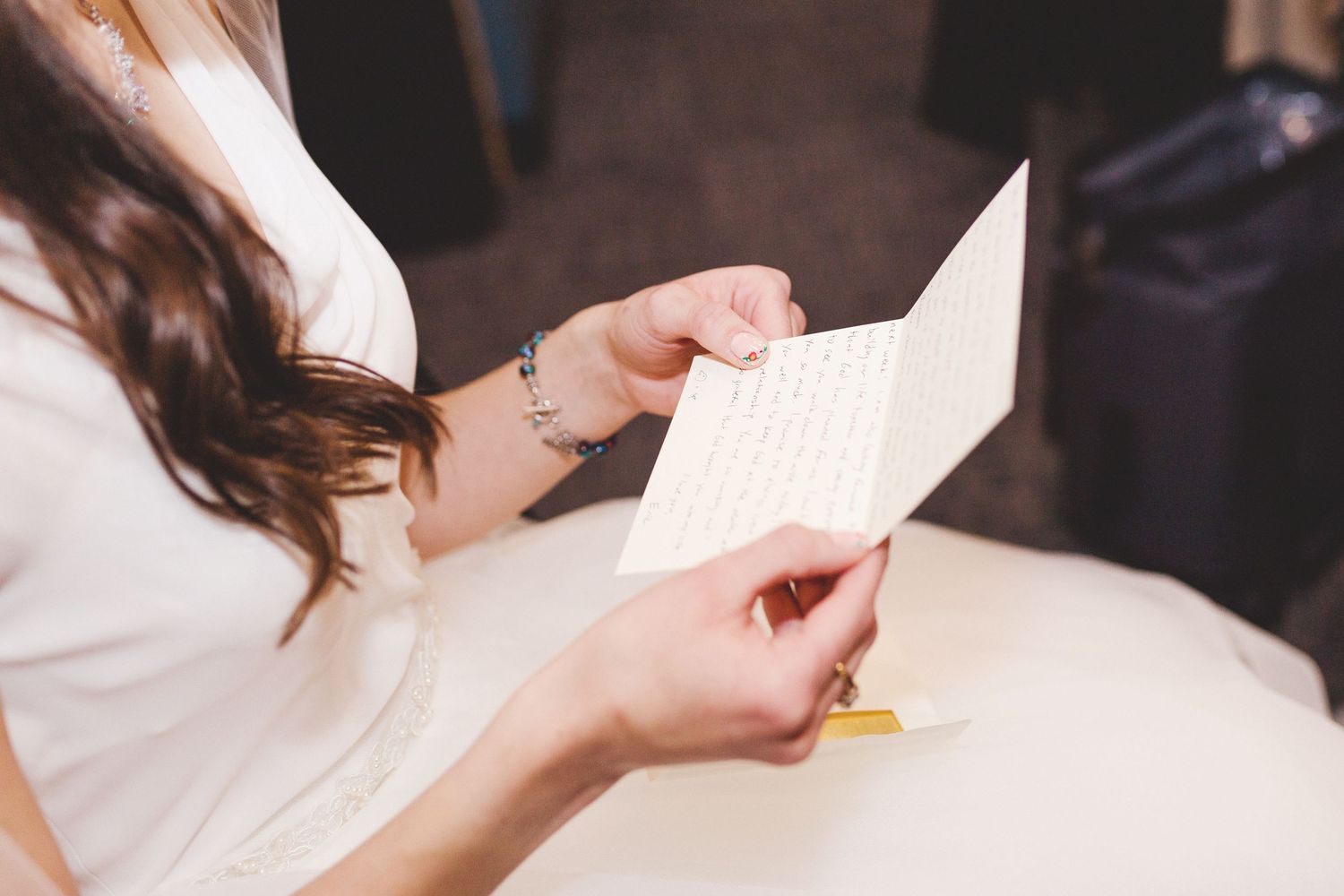 Woman in white dress reading a handwritten letter card at a table, close-up of hands holding stationery.