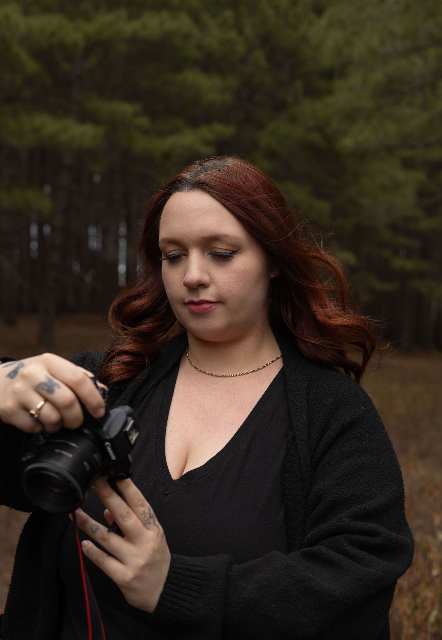 Female photographer with auburn hair reviewing shots on camera in dark forest setting.