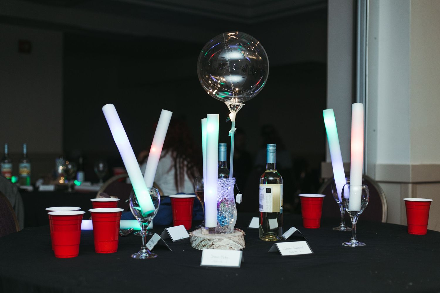 Party table with glow sticks, red solo cups, wine bottle, and disco bubble balloon centerpiece.