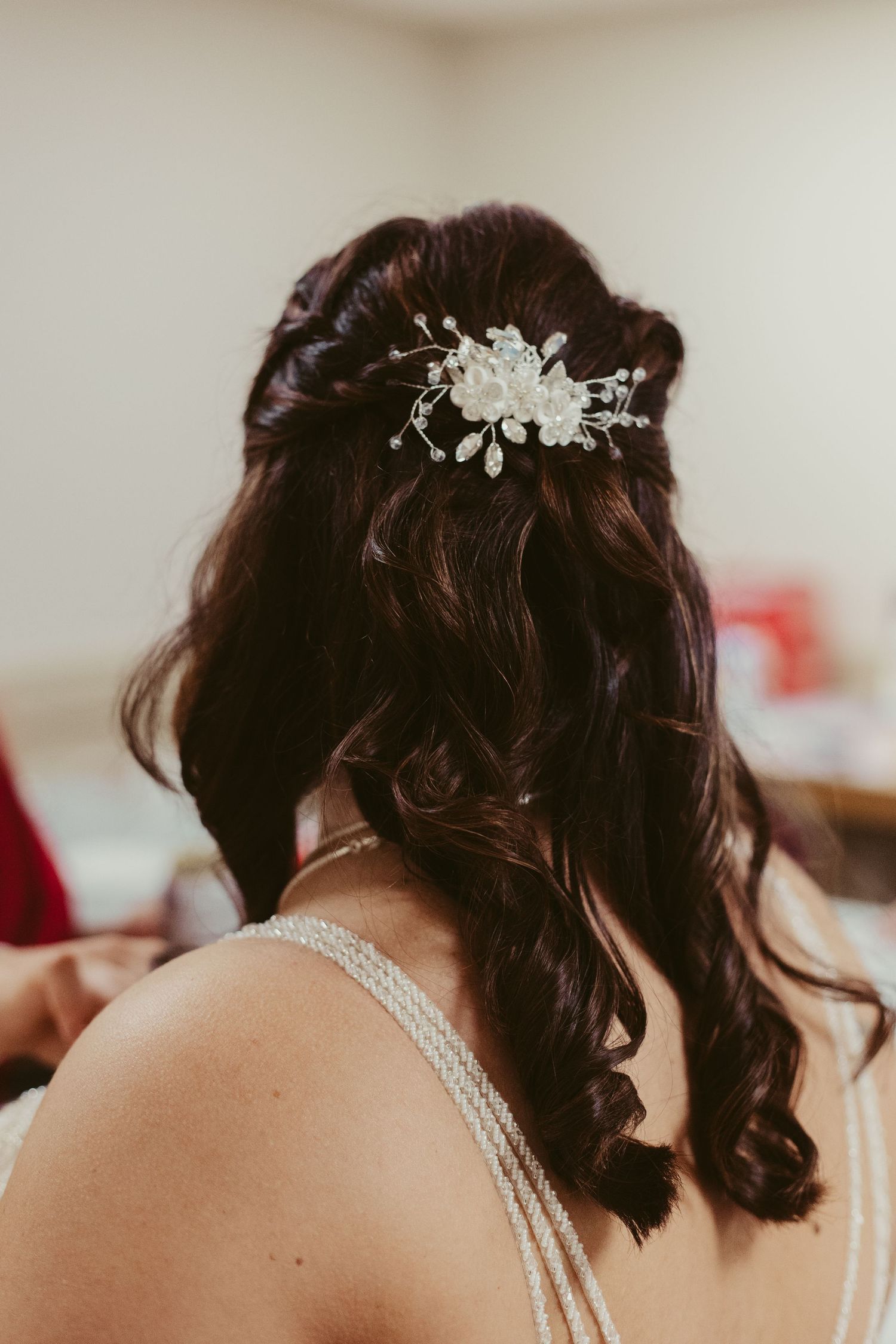 Back view of bride with dark curly hair adorned with a floral and pearl hair accessory.