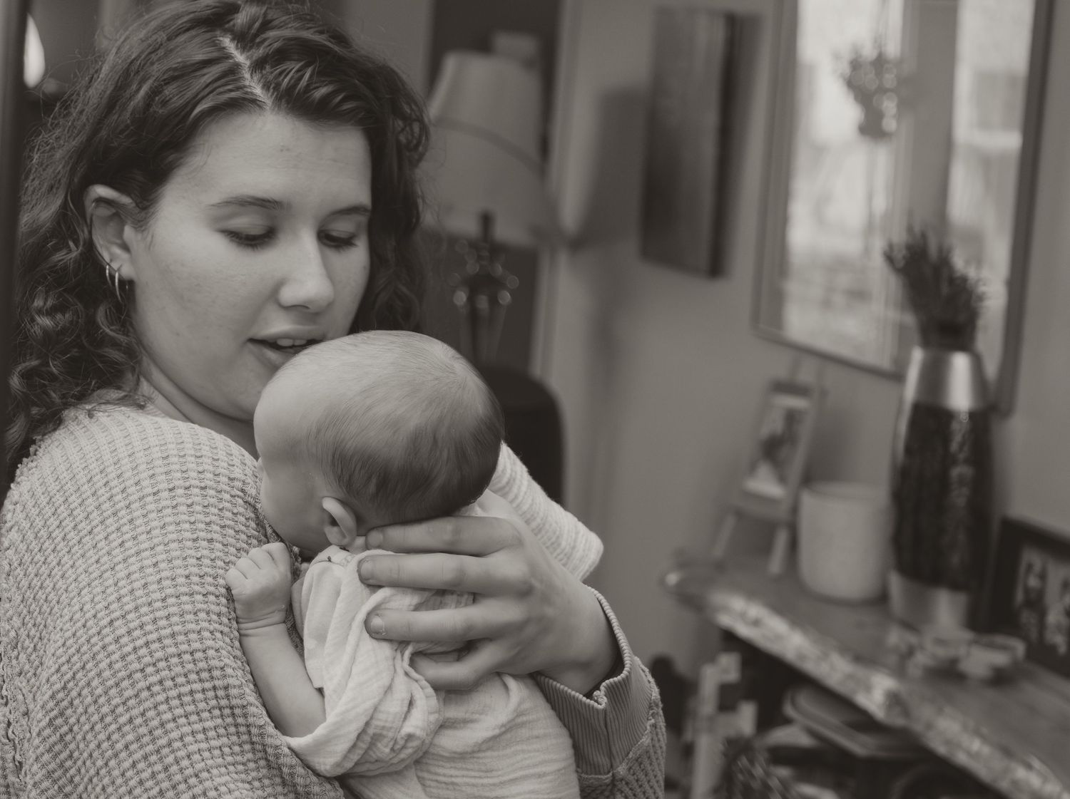 Young mother tenderly holding and gazing at her newborn baby in black and white photo.