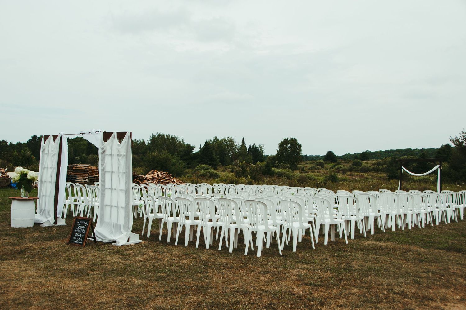 An outdoor wedding ceremony setup with white chairs and a decorative arch on a field.