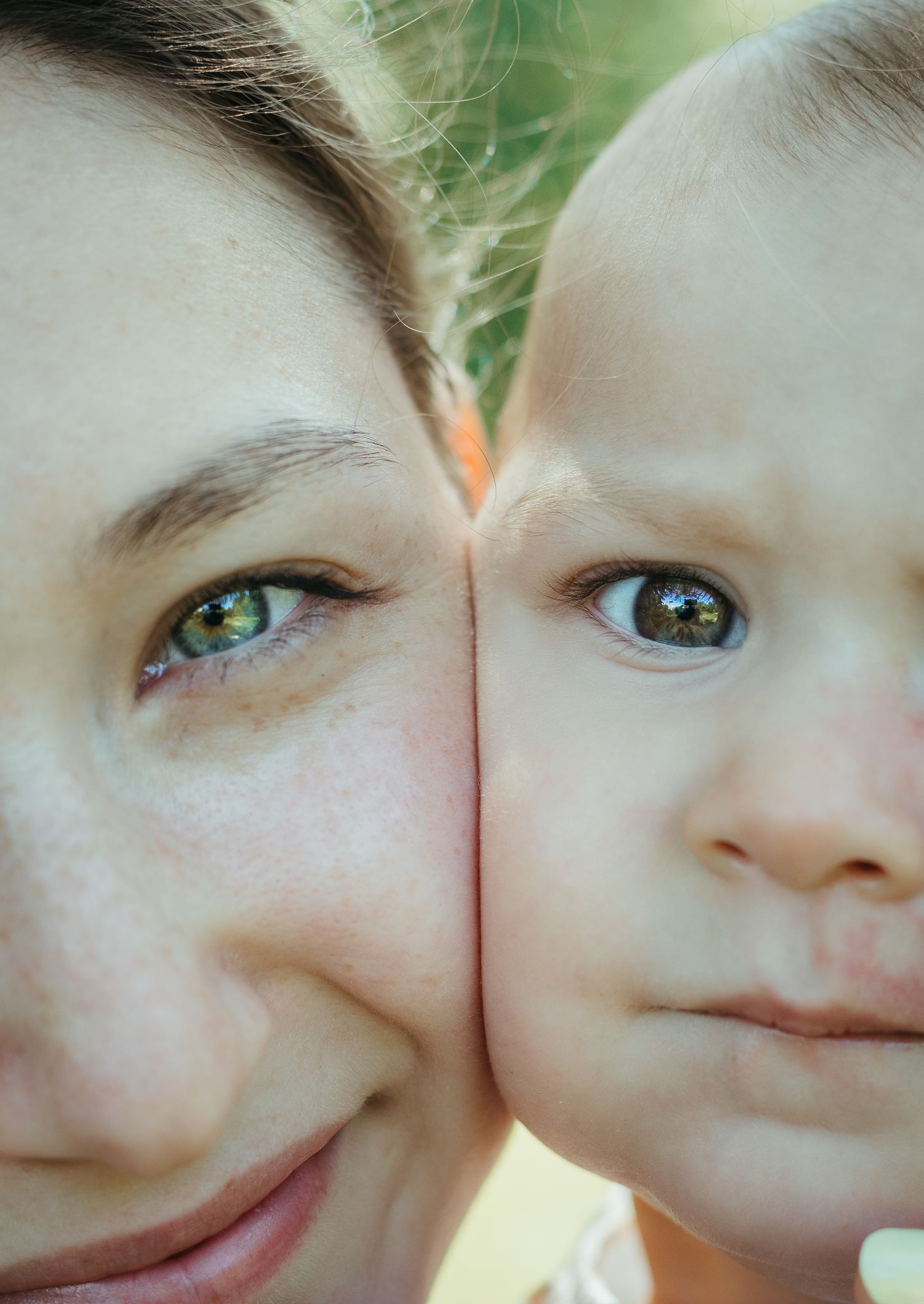 Close-up portrait of a mother and baby cheek-to-cheek, both with green-brown eyes showing family resemblance.