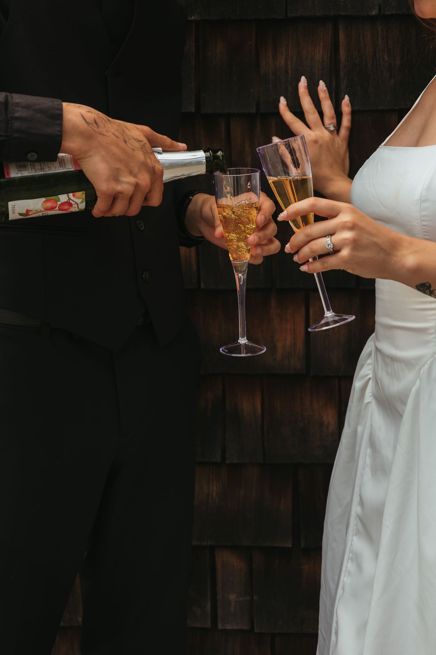Champagne being poured into flute glasses held by bride in white dress and groom in black suit.