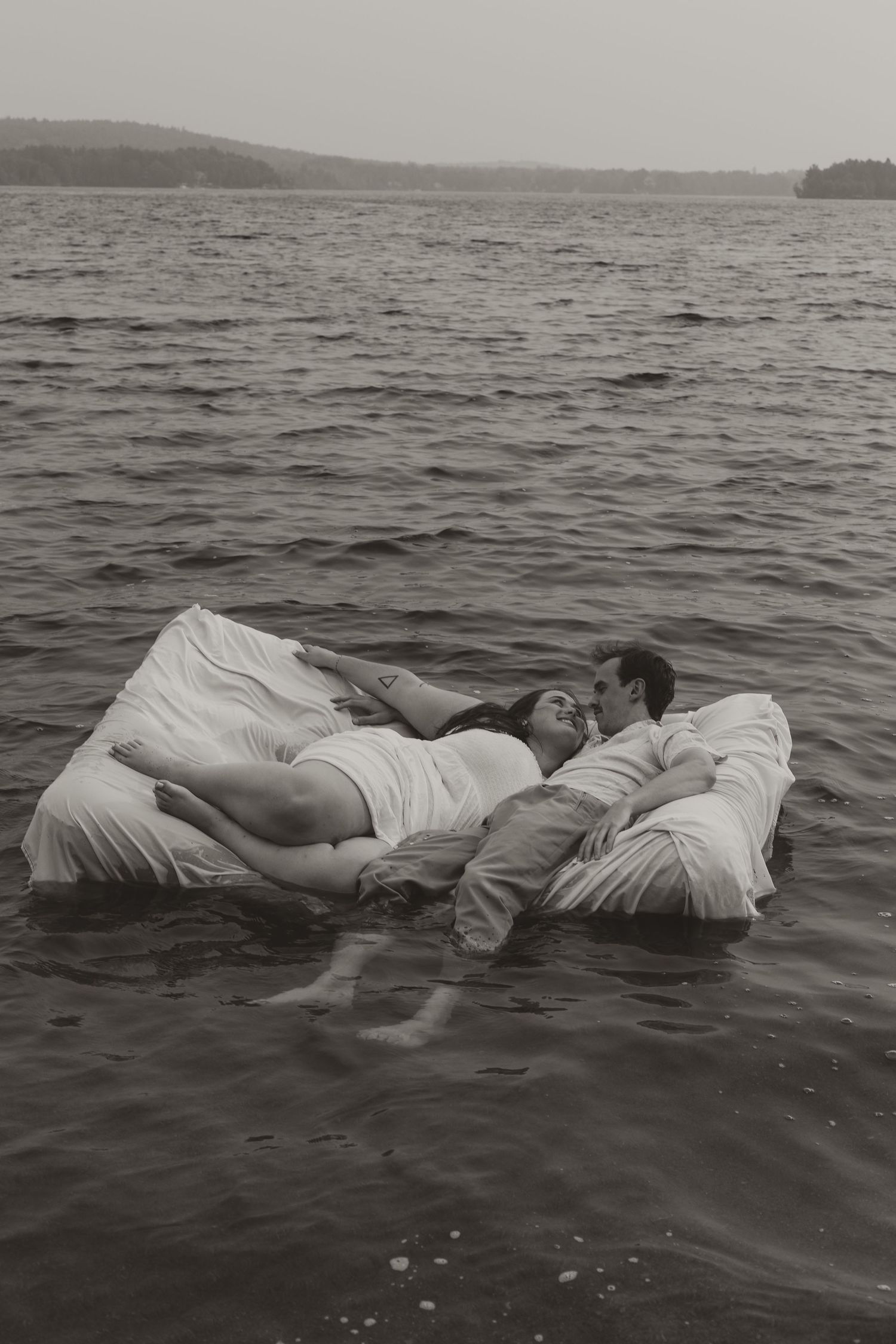 Romantic couple floating on a mattress in a lake in a black and white photo.