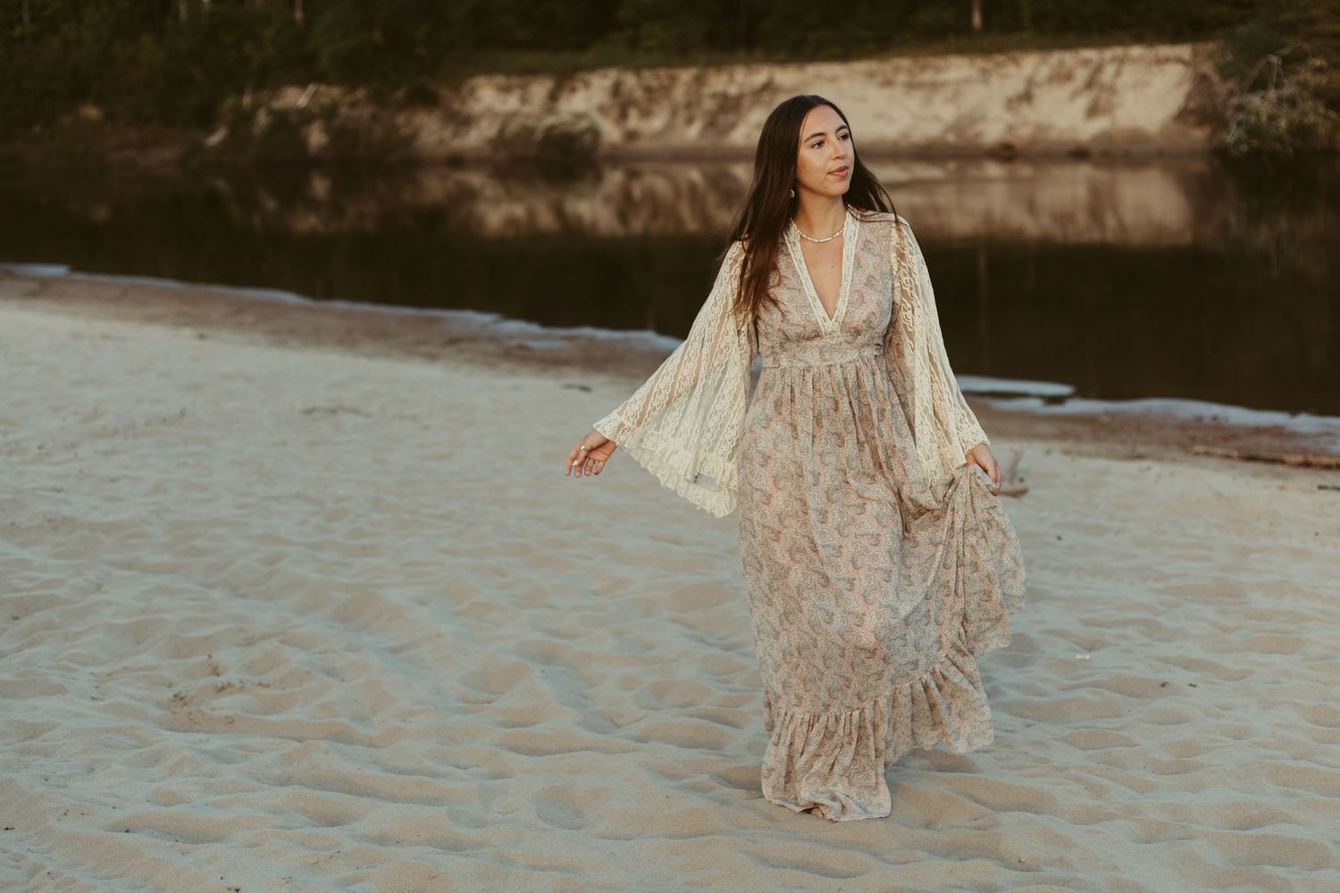 A woman in a floral boho maxi dress walks gracefully along a sandy beach at sunset.