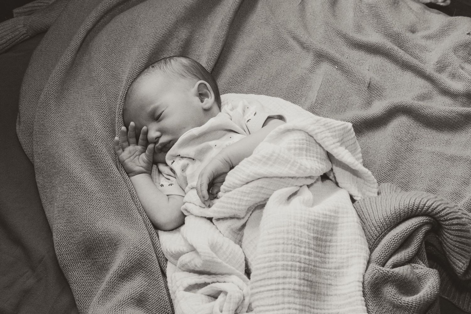 Peaceful newborn baby sleeping on soft blankets in black and white photography.
