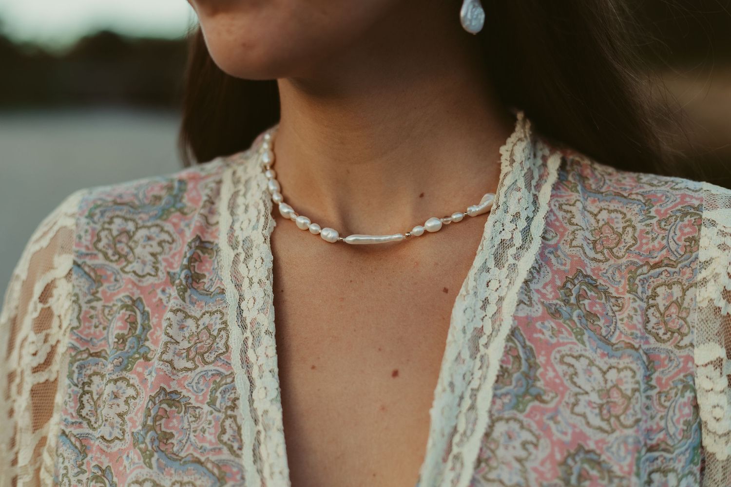 Close-up of a woman wearing a delicate pearl choker necklace and floral lace blouse.