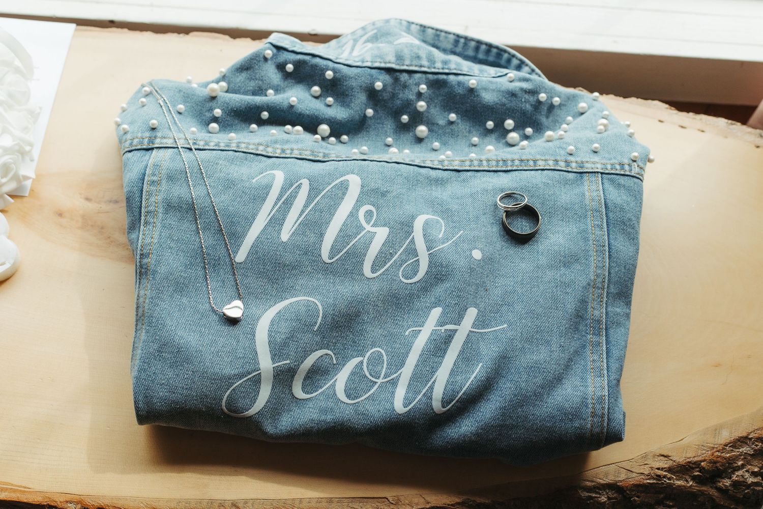 Custom pearl-embellished denim jacket reading Mrs. Scott displayed with wedding rings.