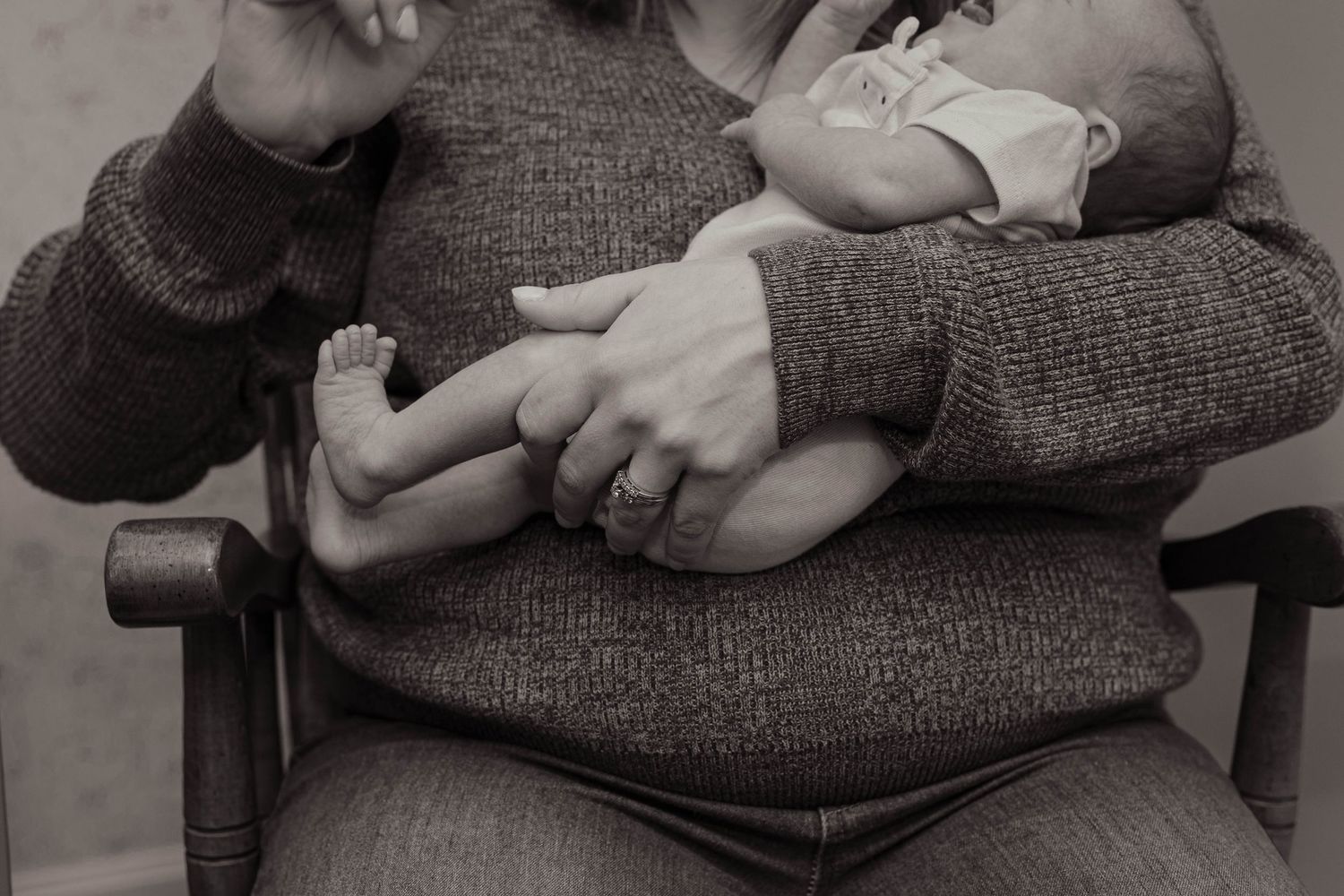 Black and white photo of a parent cradling a newborn baby in their arms while seated in a chair.