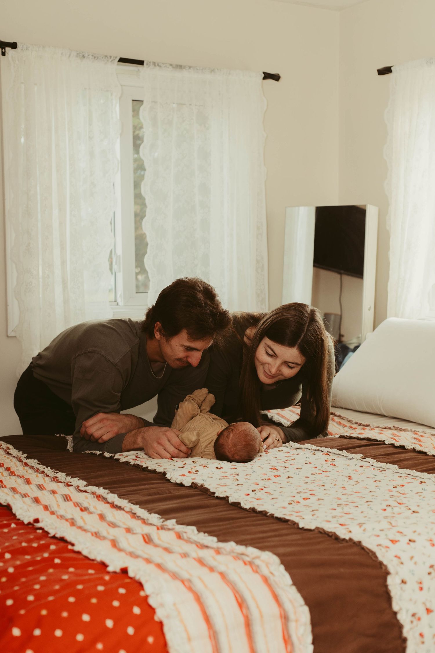 New parents lying on bed gazing lovingly at their newborn baby on a colorful quilt.