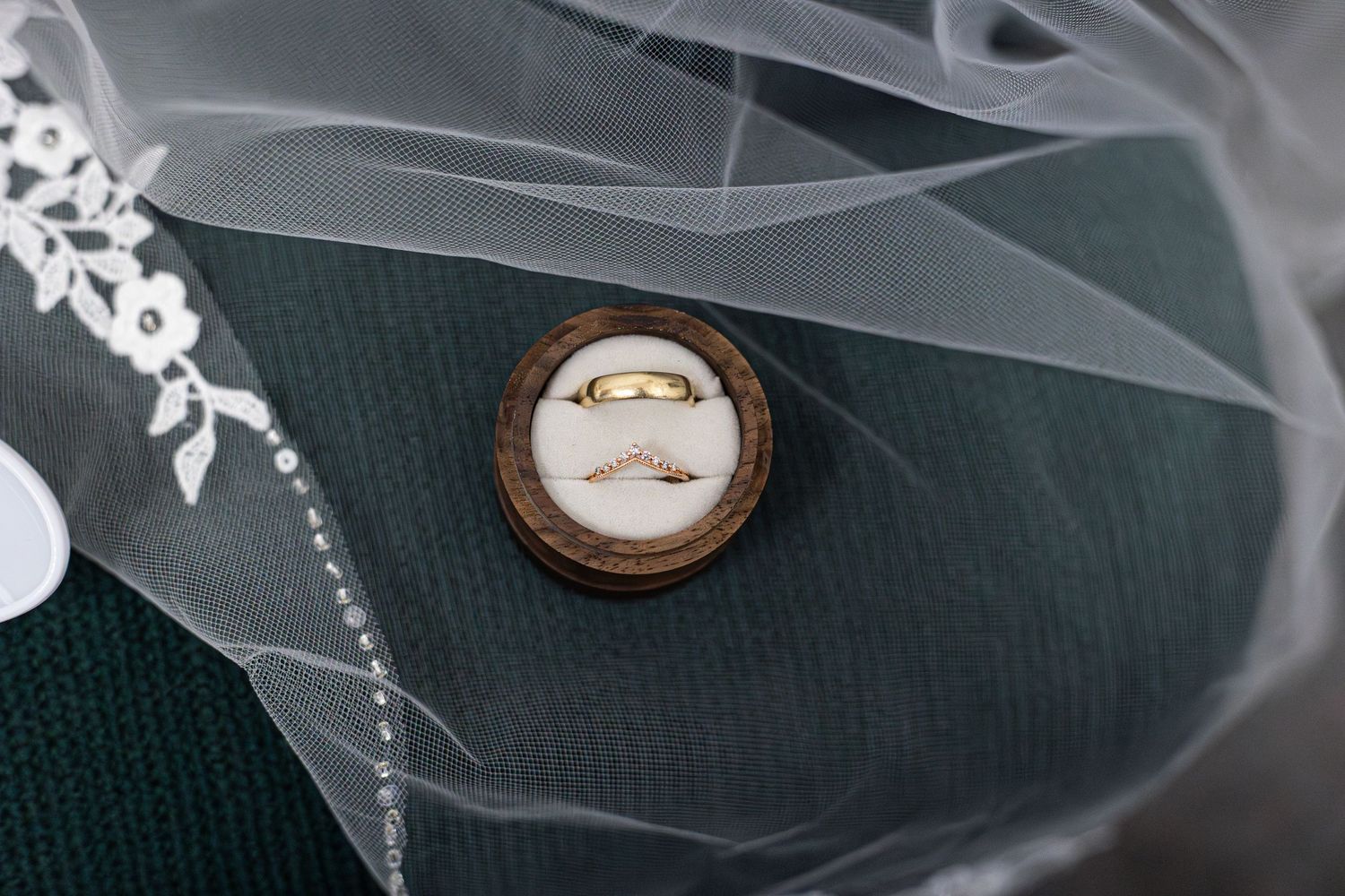 Two gold wedding bands displayed in rustic wooden ring box with white velvet lining and bridal veil.