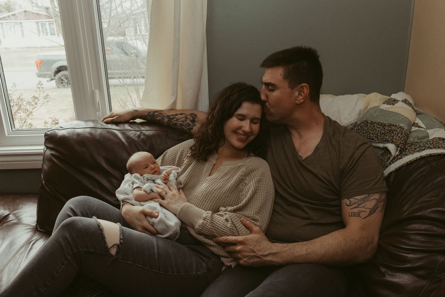 Happy couple sitting on couch sharing tender moment with their newborn baby at home.