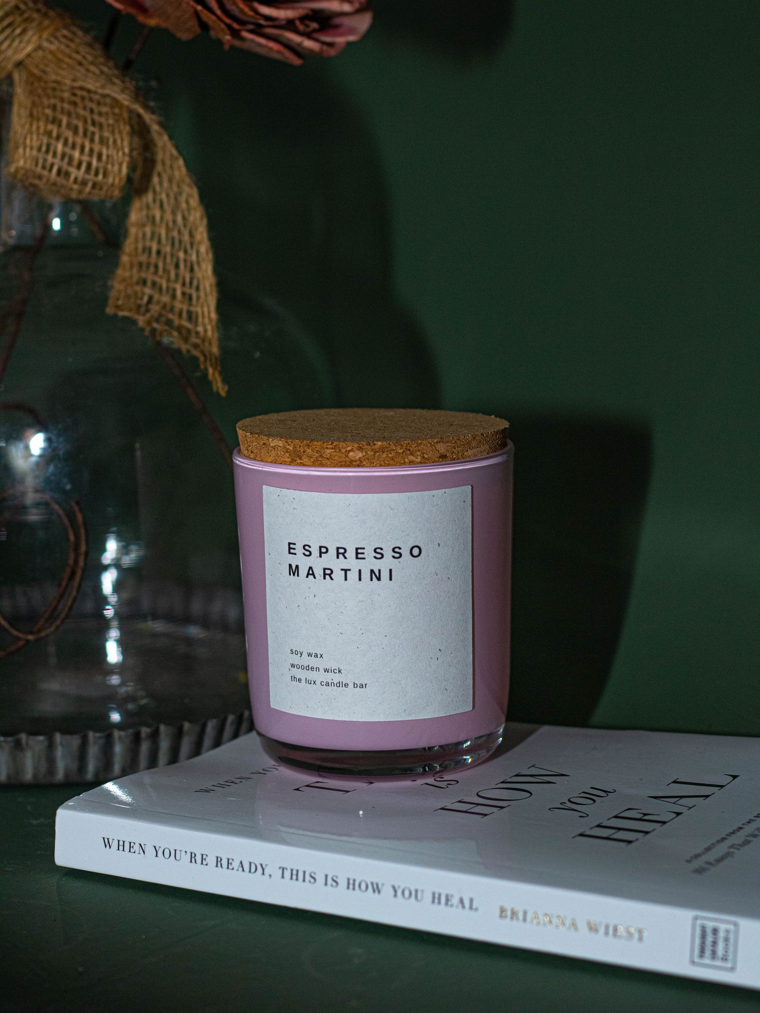Espresso Martini scented candle in lavender jar with cork lid on top of a self-help book.