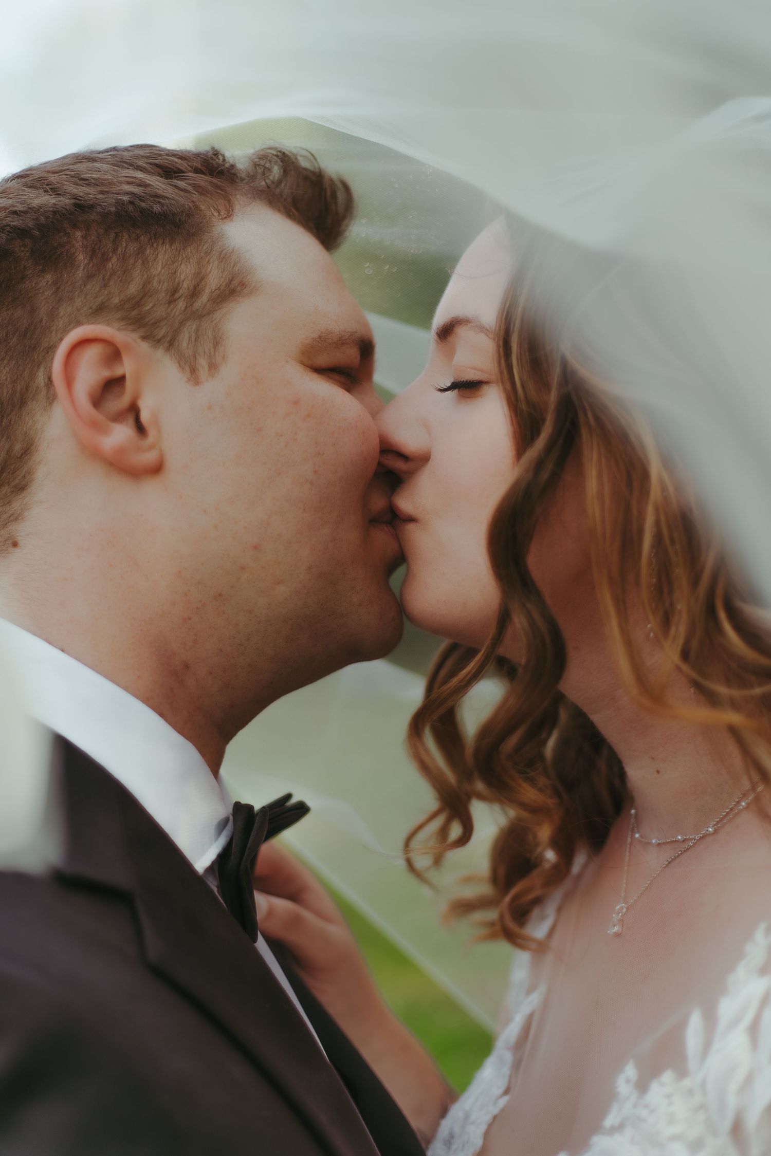 Bride and groom sharing romantic kiss under wedding veil in close-up portrait.