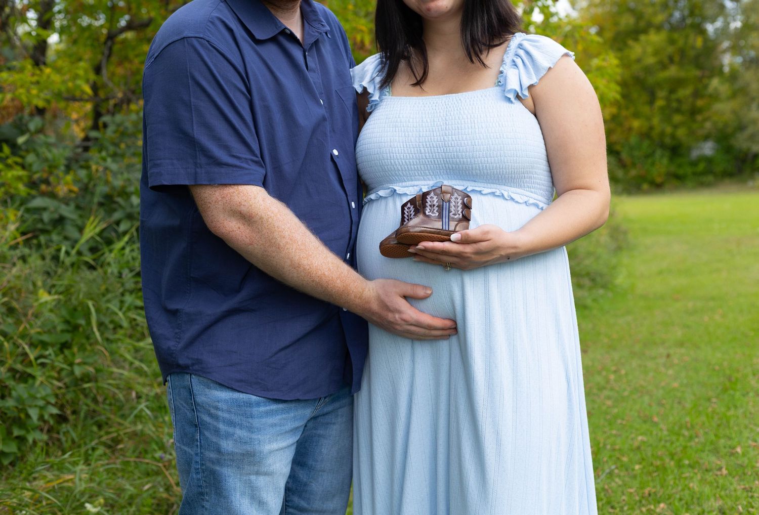 Couple holding ultrasound photo during outdoor maternity photoshoot, woman in light blue dress cradling baby bump.