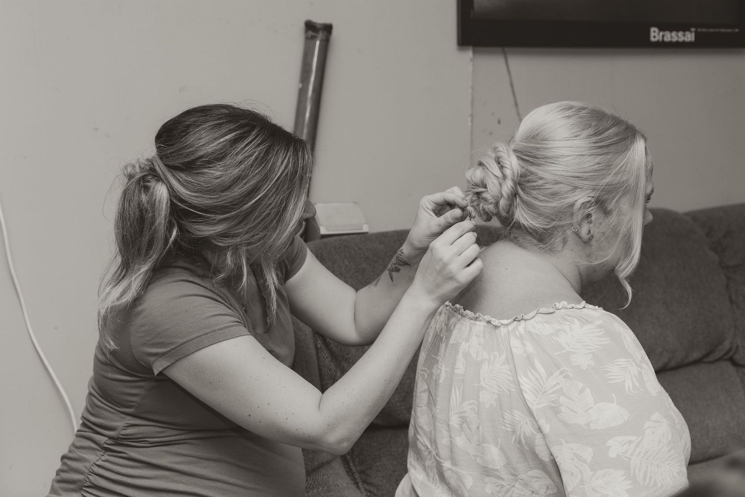 Black and white photo of a woman styling another womans elegant updo hairstyle for a wedding.