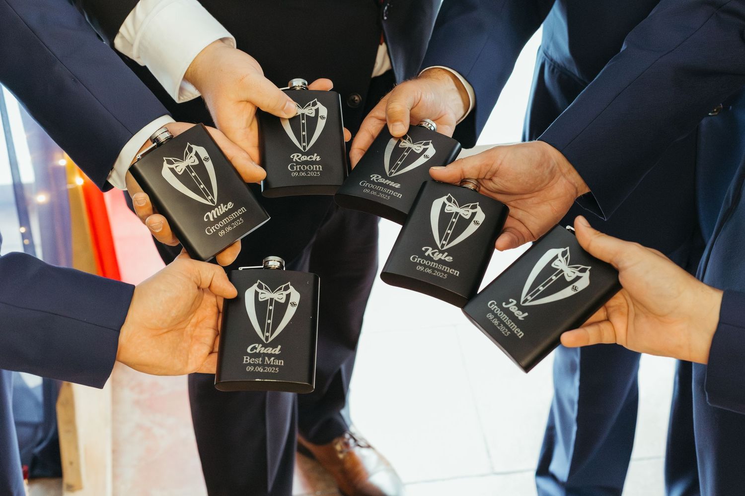 Groomsmen holding personalized black flask wedding party gifts with tuxedo design in a circle.