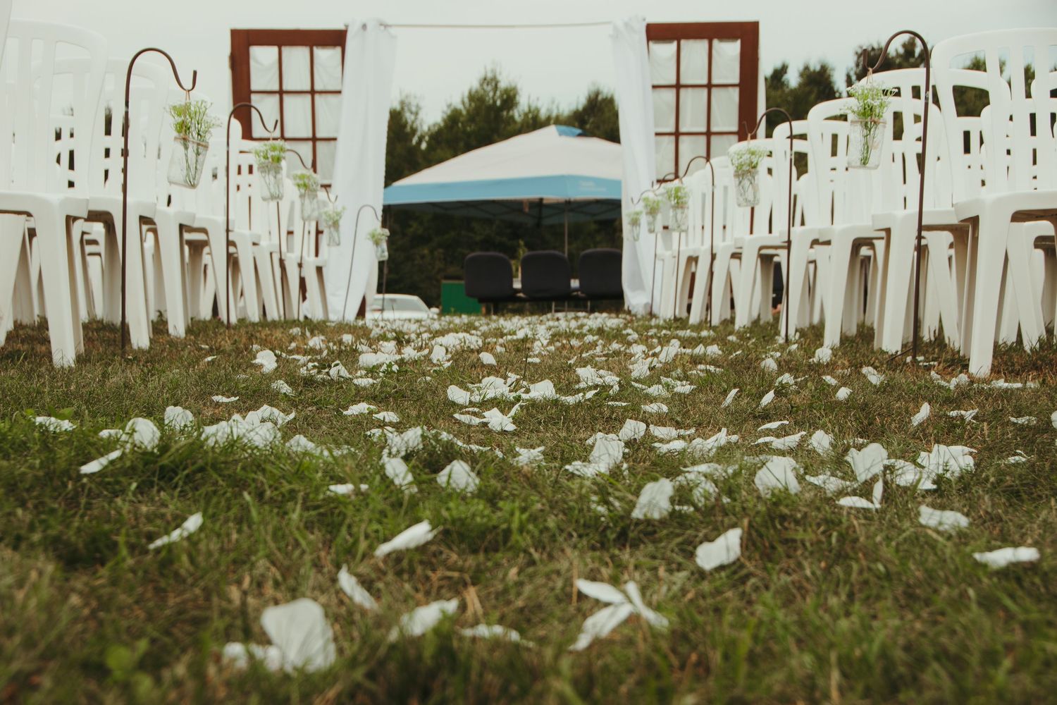 White flower petals scattered on grass along a wedding ceremony aisle with white chairs.