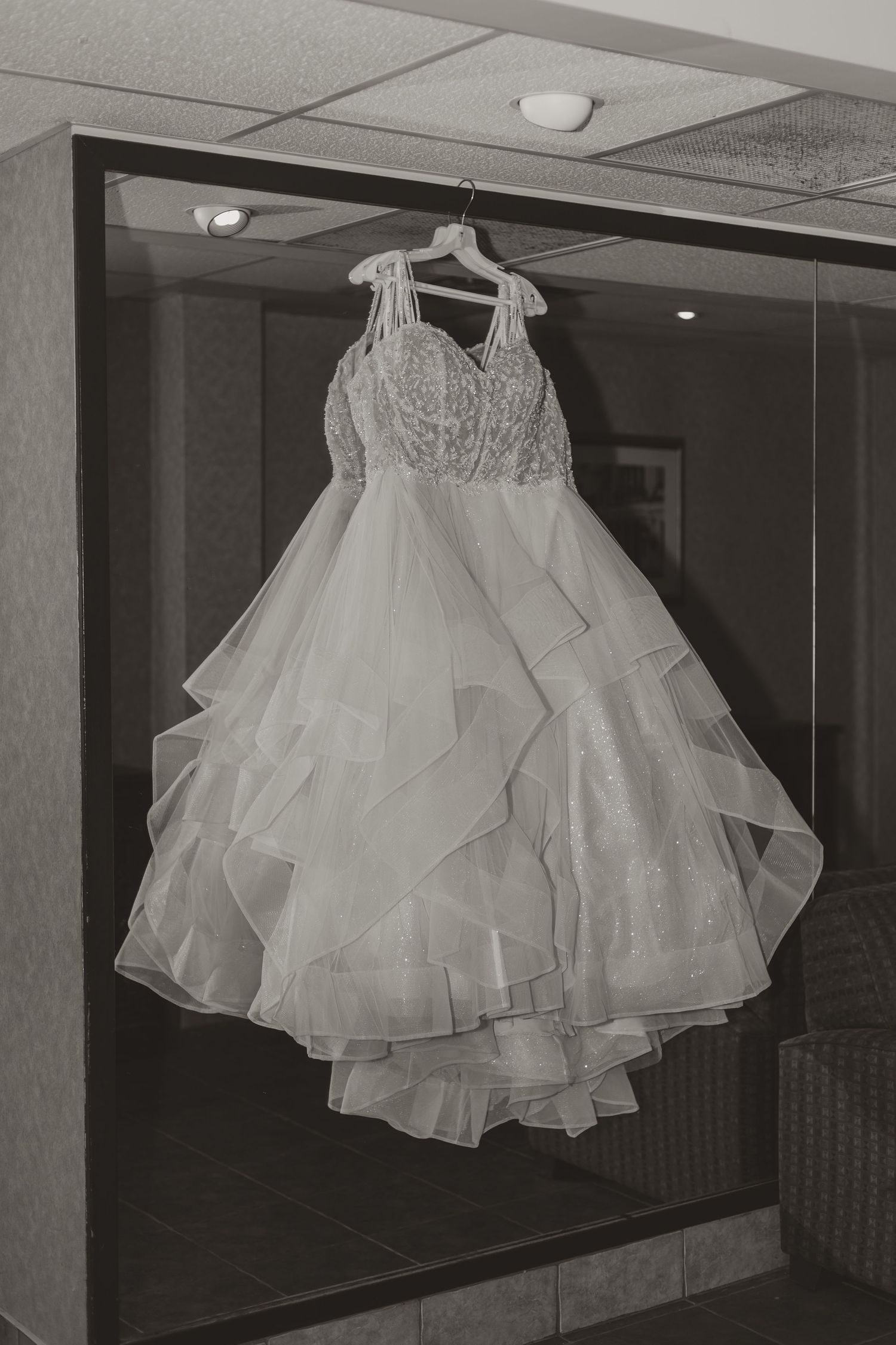 Elegant white layered ballgown wedding dress with lace bodice hanging on hanger in black and white.
