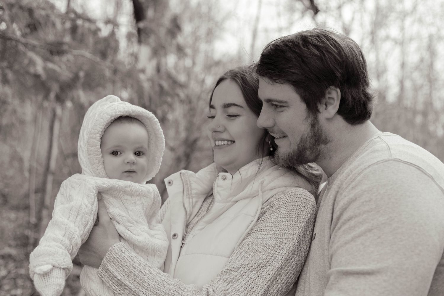 Young family shares a tender moment outdoors in a black and white portrait with their baby.