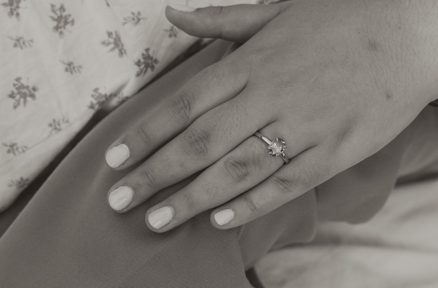 Close-up of an engagement ring with a diamond on a woman's hand in black and white.