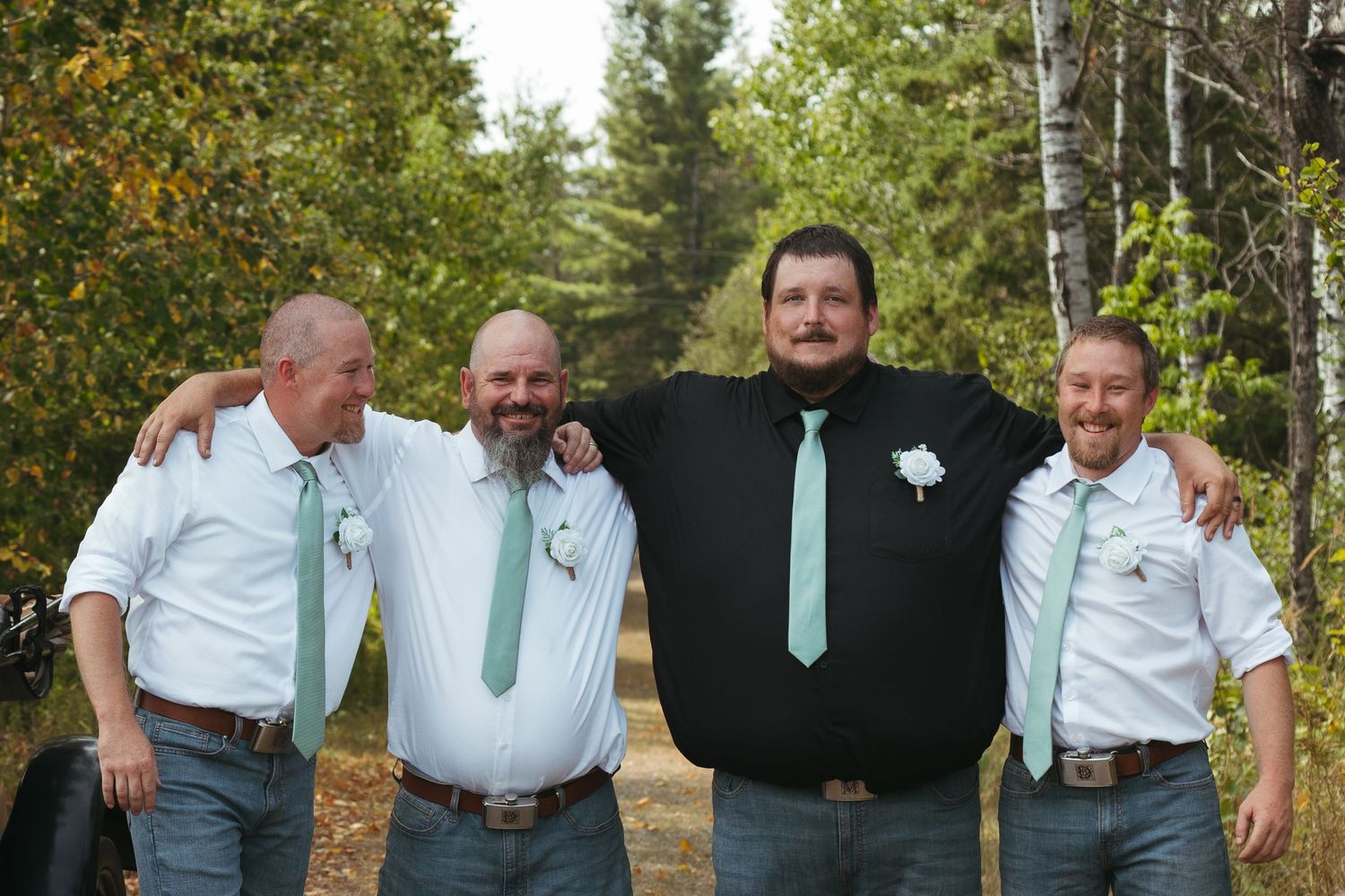 Groom and groomsmen in mint ties smiling together in birch tree forest.