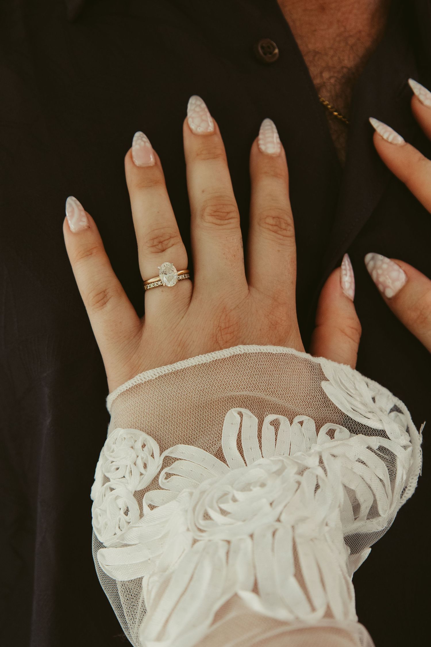 Close-up of bride's hand showing diamond engagement ring and wedding band with lace sleeve detail.