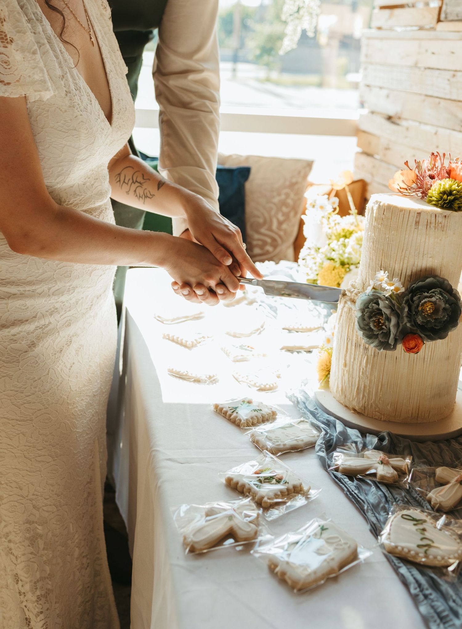 Bride and groom cutting wedding cake at elegant reception table with decorated sugar cookies and floral cake topper.