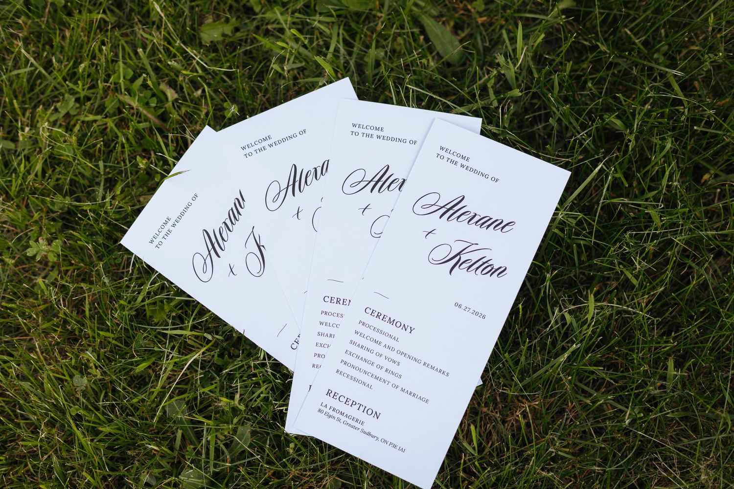 Elegant wedding programs with calligraphy script displaying couple names Alex and Alexne fanned out on green grass.