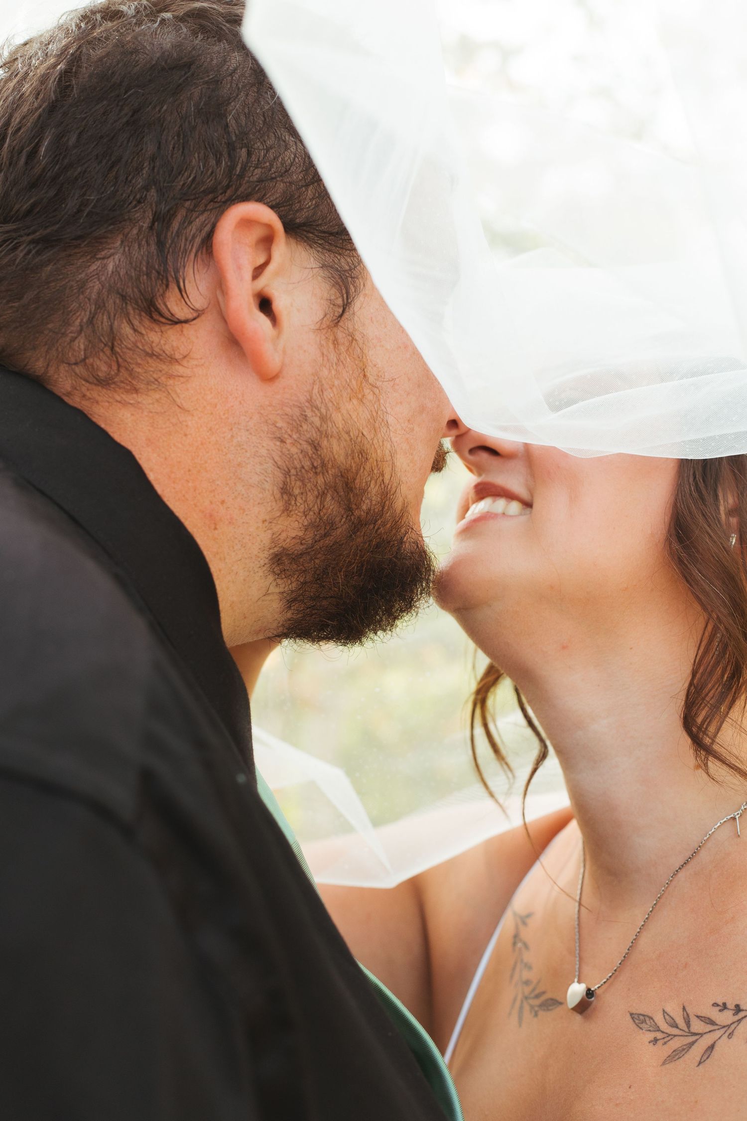 A bearded groom and smiling bride share a romantic moment under her wedding veil.