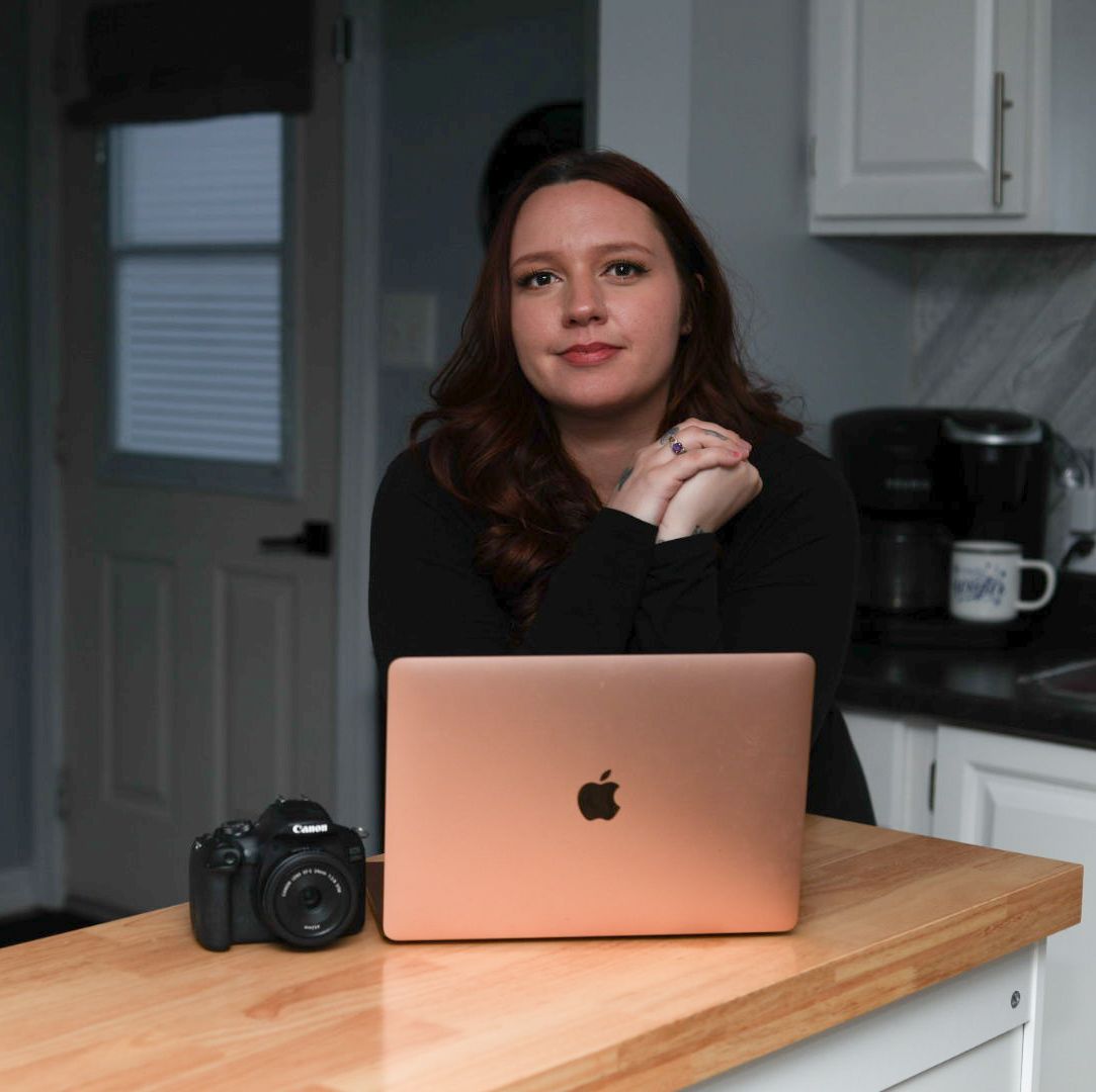 Young female photographer posing at kitchen island with rose gold MacBook and Canon DSLR.